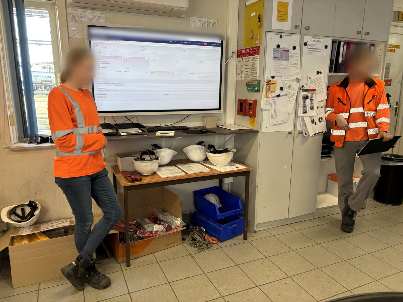 Een groot scherm met het digitale bord in een controlekamer. Twee medewerkers in werkkledij staan ervoor.